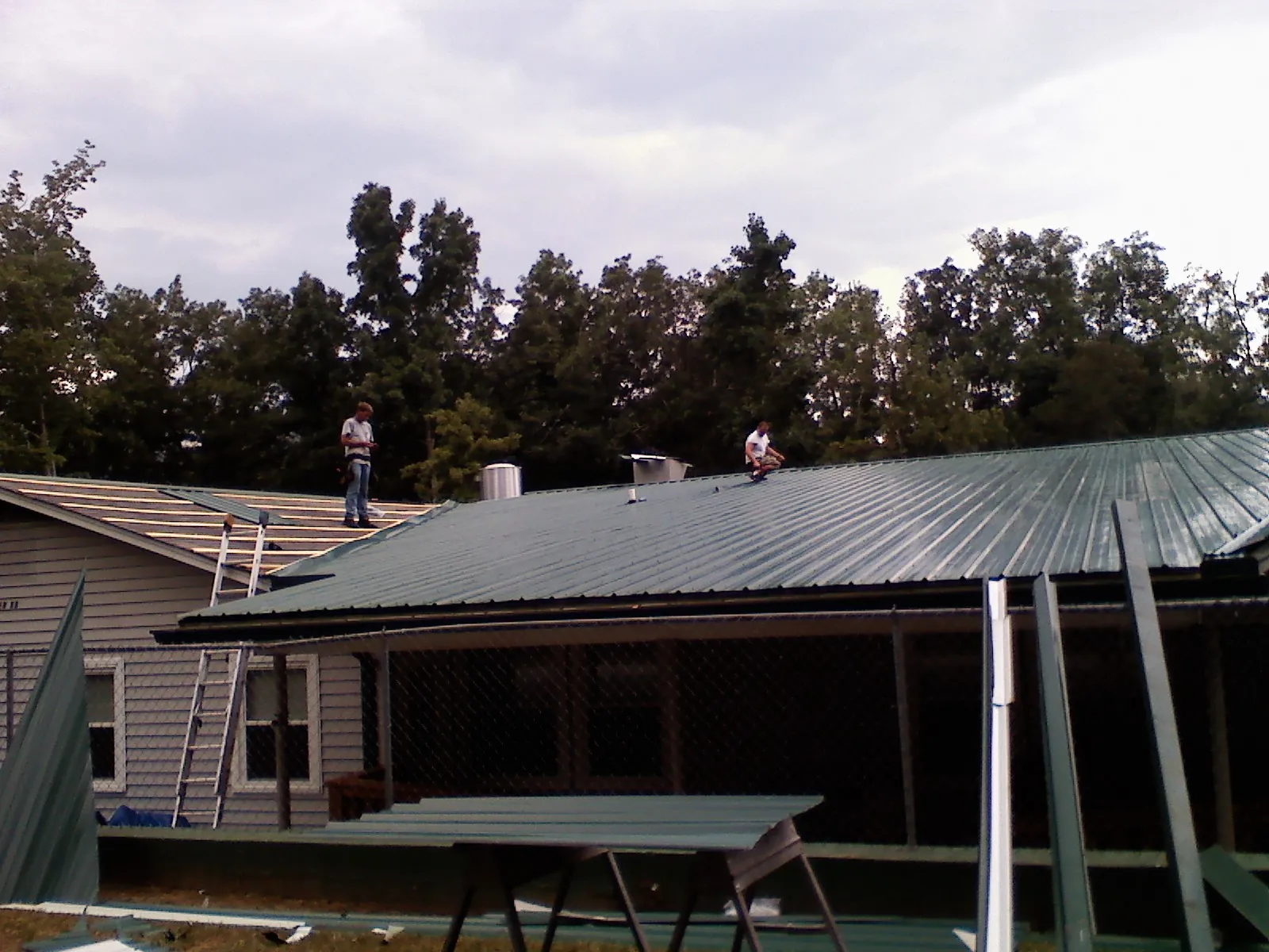 Two roofers installing green metal panels above a covered porch in Saint Charles